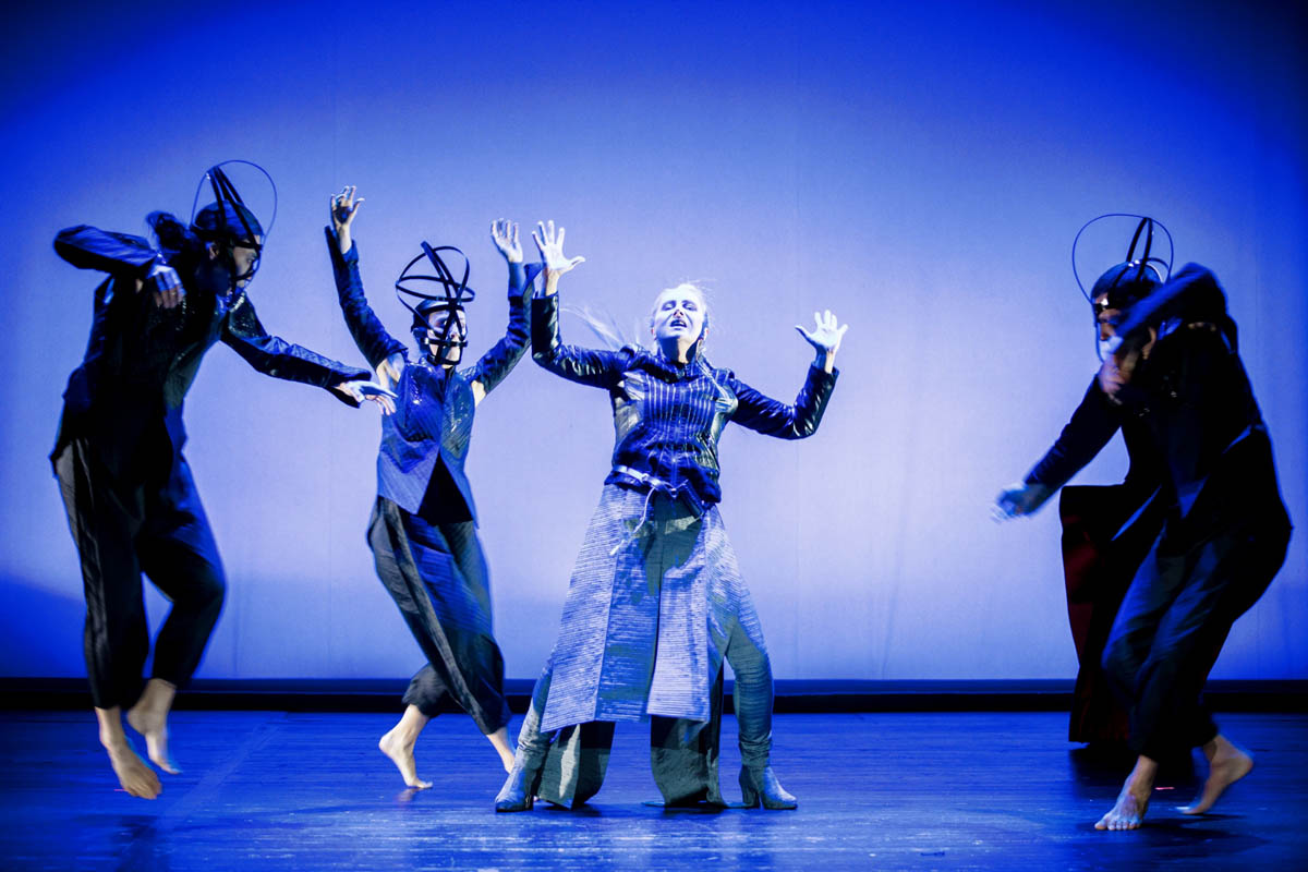 Cztery postacie w dużych nakryciach głowy i w obcisłych strojach ukazane w dynamicznym ruchu.