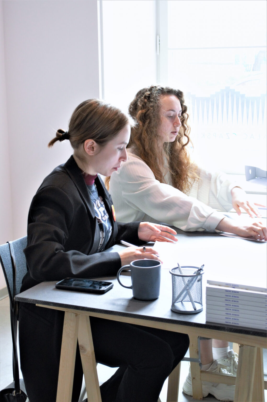 Dwie kobiety siedzące przy stoliku sporządzają notatki