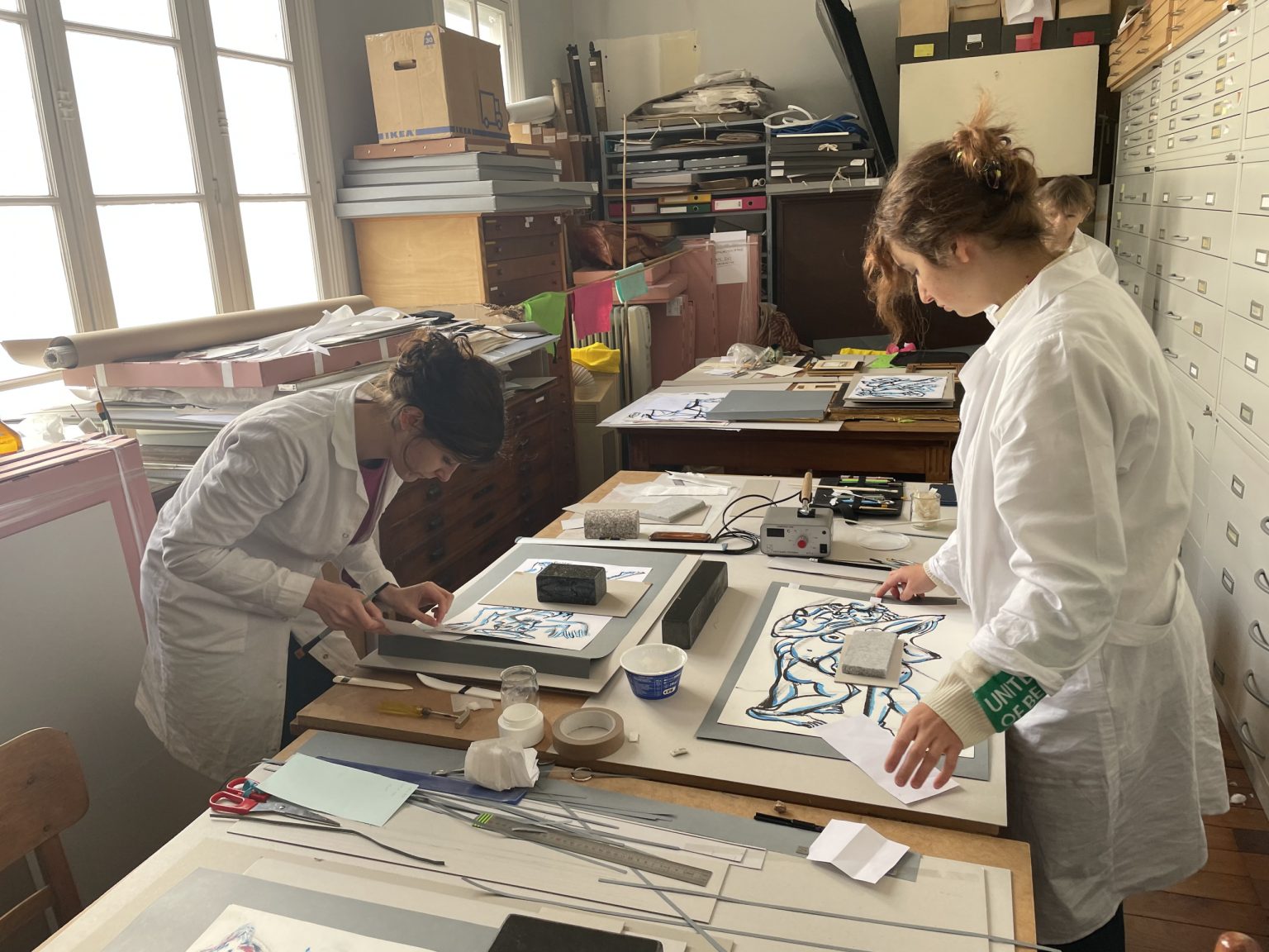 Dwie studentki pochylone nad stołem wykonują prace konserwacyjne