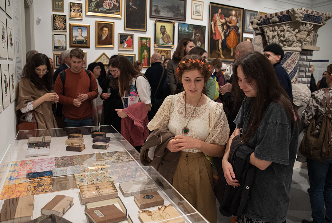 Publiczność w sali wystawowej obserwuje dzieła eksponowane na ścianach i w gablotach