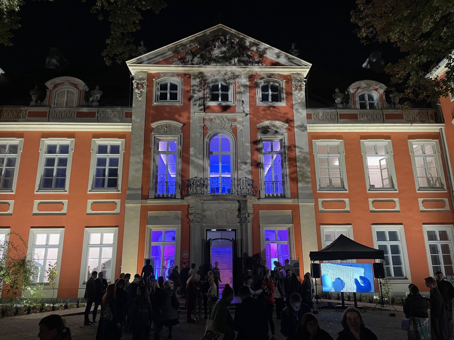 Iluminowana fasada Pałacu Czapskich. Wnętrze hallu głównego oświetloneniebiesko-różowym światłem