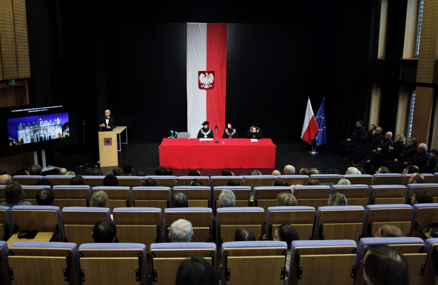 Aula główna ASP w Warszawie. Na scenie za czerwonym stołem siedzą przedstawiciele władz uczelni.