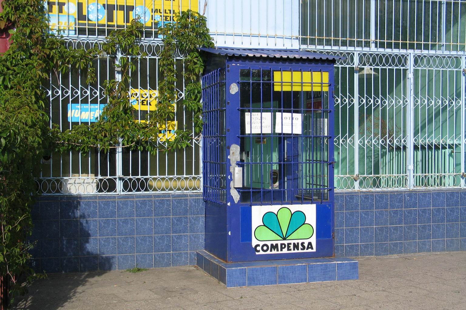 Wejście do sklepu. W oknach zainstalowane są kraty, przez okna widać nie używane wnętrze