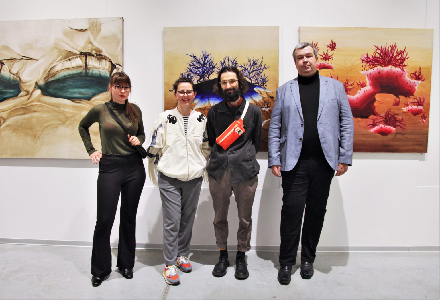 2 mężczyzn oraz dwie kobiety pozują do zdjęcia stojąc przed ścianą z zawieszonymi obrazami