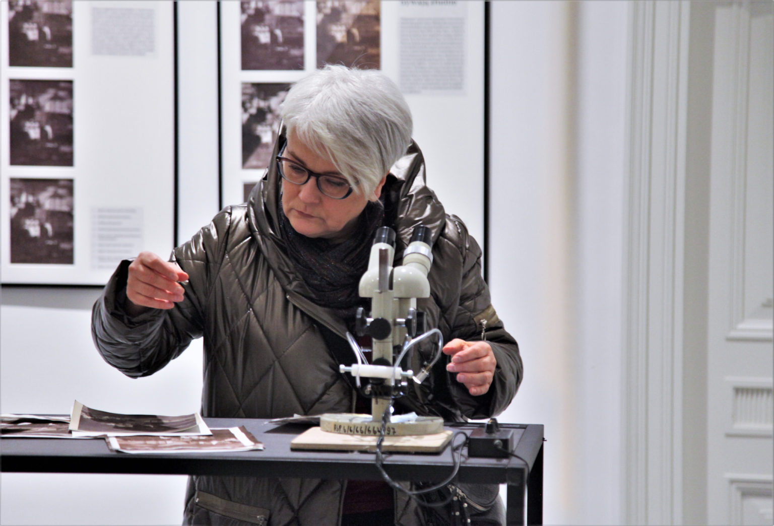 Kobieta stoi przy wysokiej ławie z ustawionym na niej mikroskopem