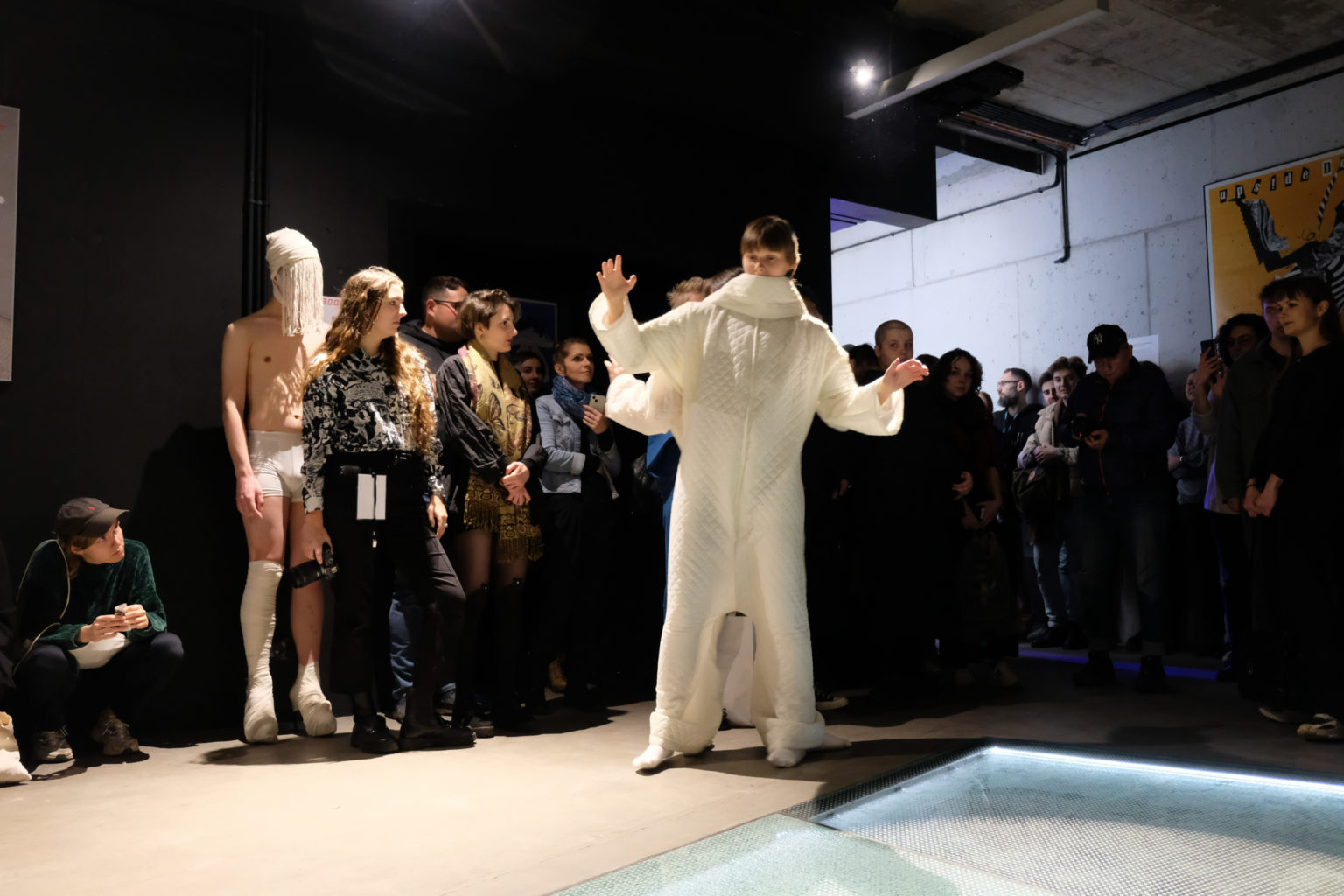 Performance. Dwie osoby w białym kostiumie otoczone przez stojącą publiczność.