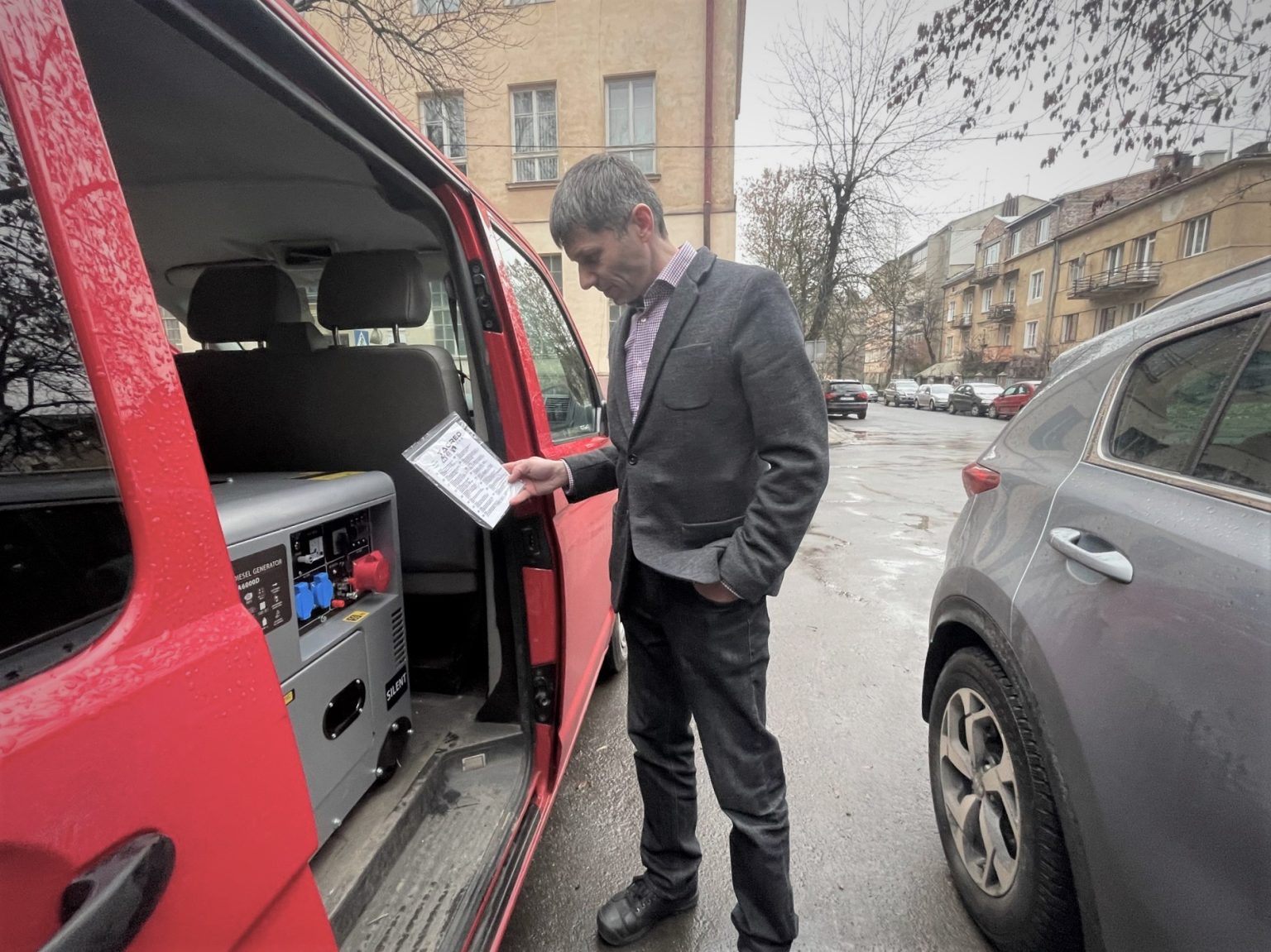 Mężczyzna patrzy na załadowane do samochodu urządzenie. W ręku trzyma dokumenty.