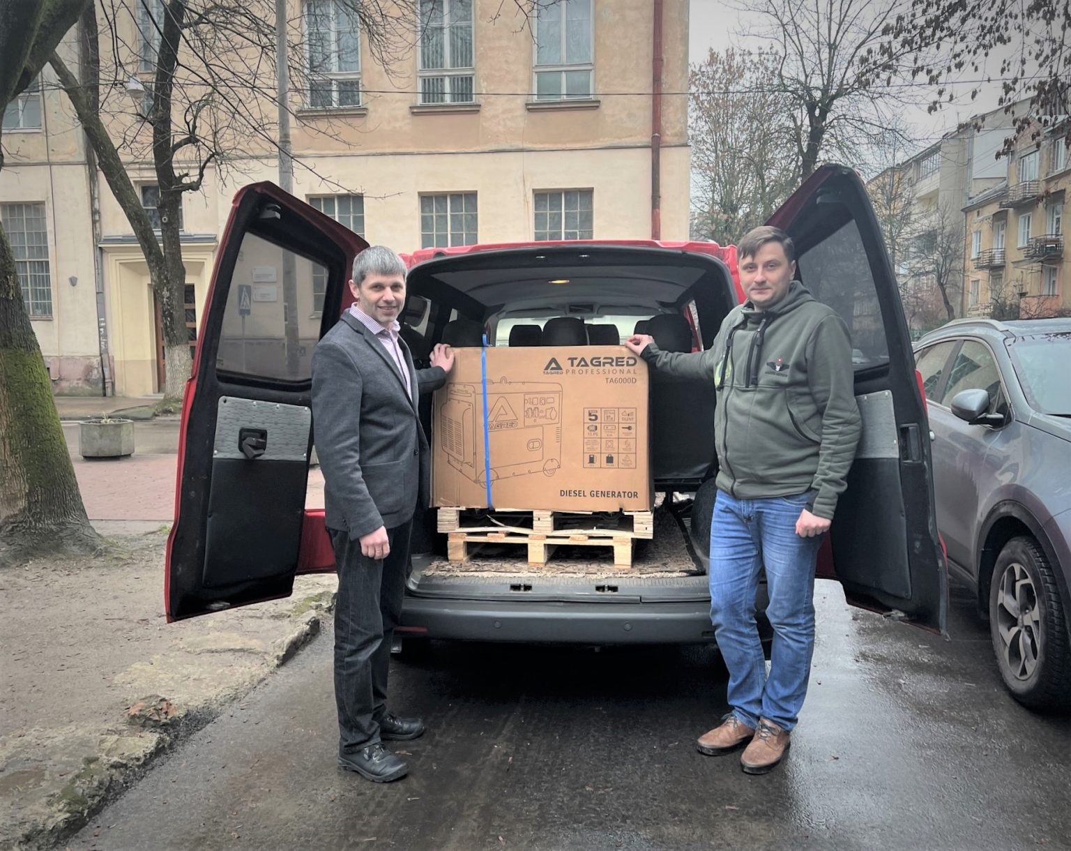 Dwóch mężczyzn pozuje do zdjęcia, opierając dłonie na załadowanym do samochodu urządzeniu