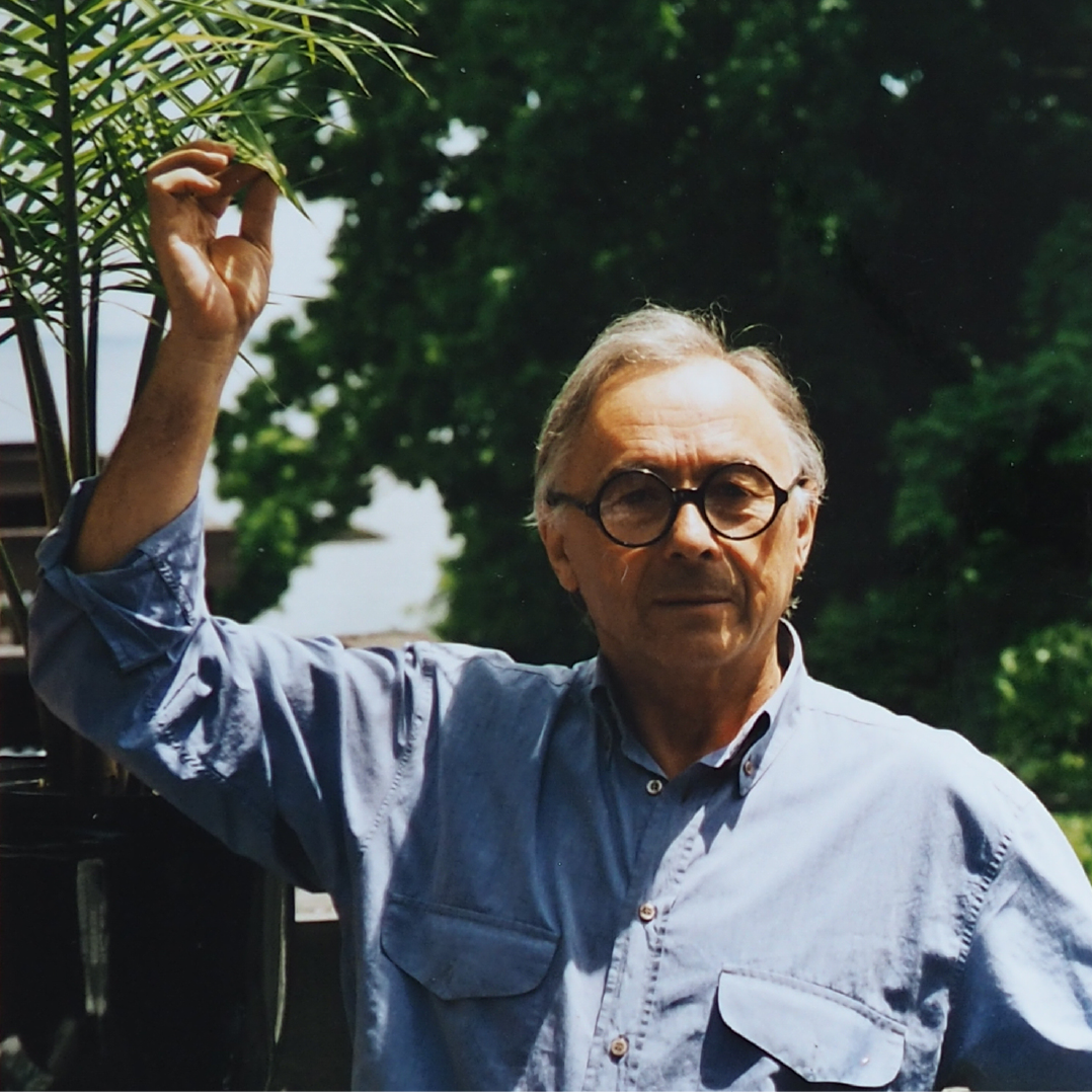 Artysta trzyma palmę, dotykając liścia, jakby zbliżając się, by się jej dokładniej przyjrzeć.