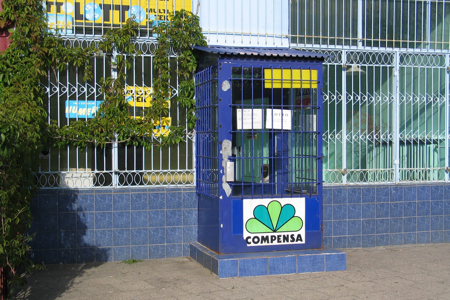 Wejście do sklepu. W oknach zainstalowane są kraty, przez okna widać nie używane wnętrze