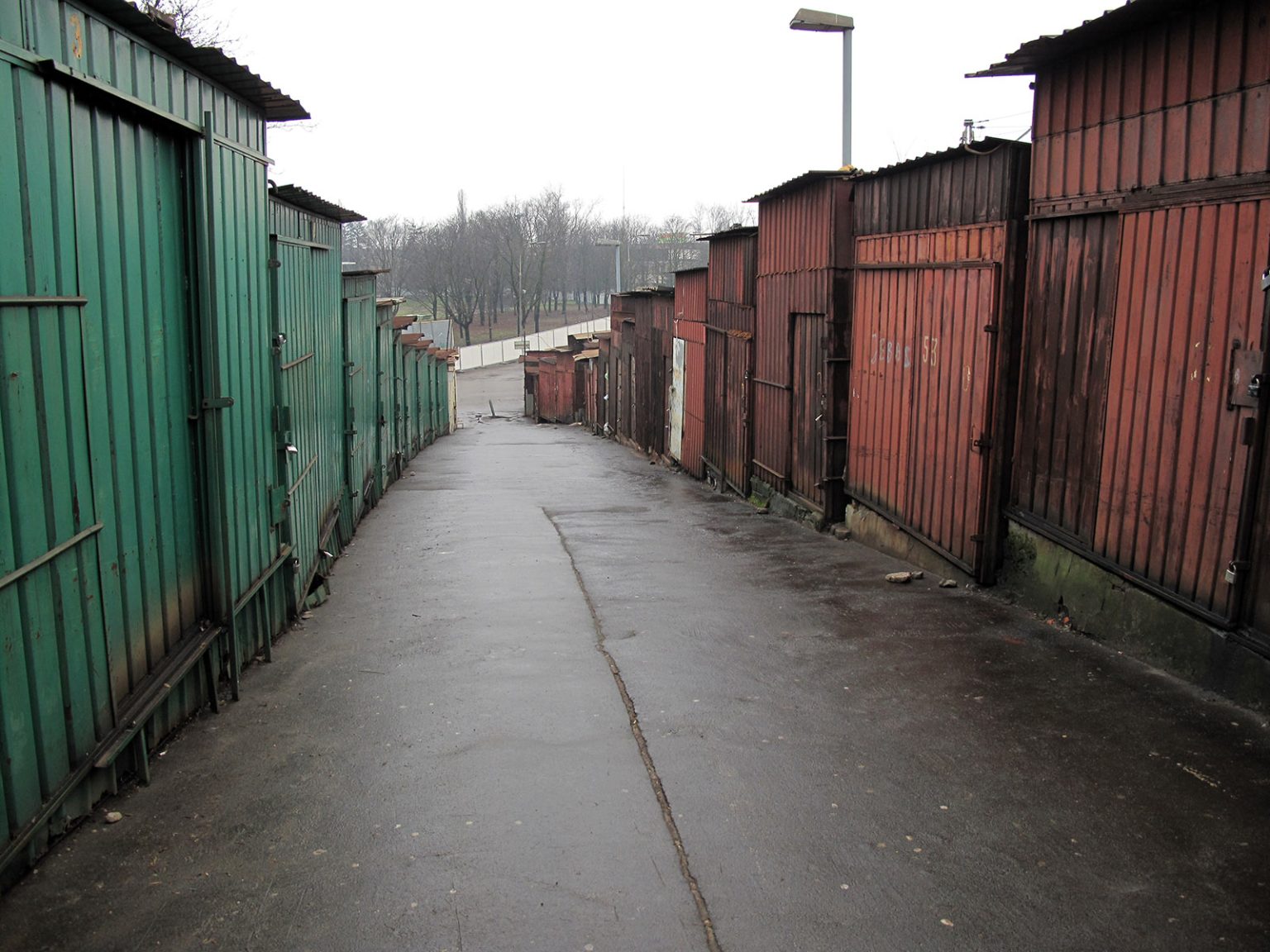 Wzdłuż alejki stoją na betonowych, zmurszałych stopniach pozamykane wiaty stoisk handlowych bazaru.