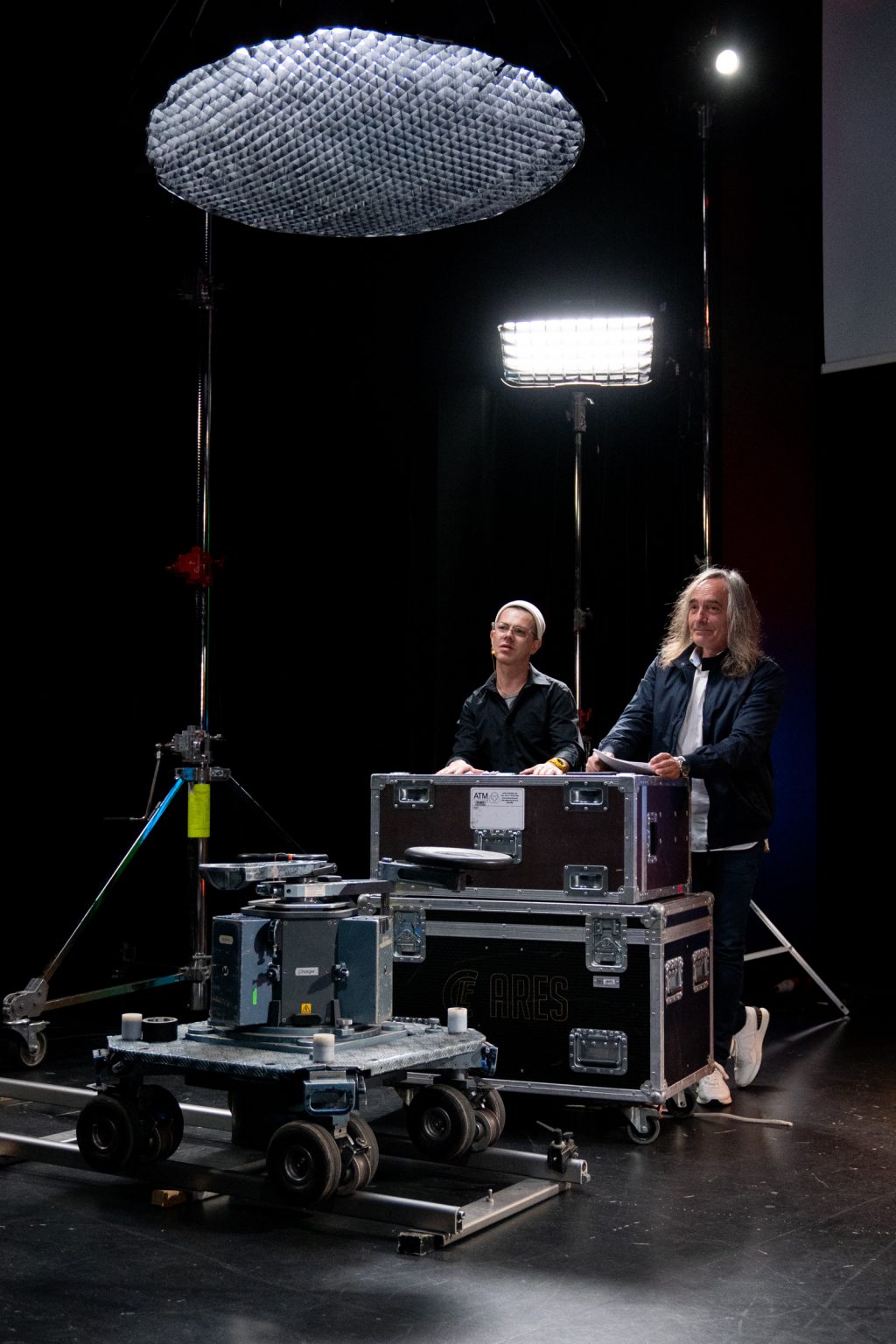 Dwie osoby stoją oparci o sprzęt z planu filmowego.