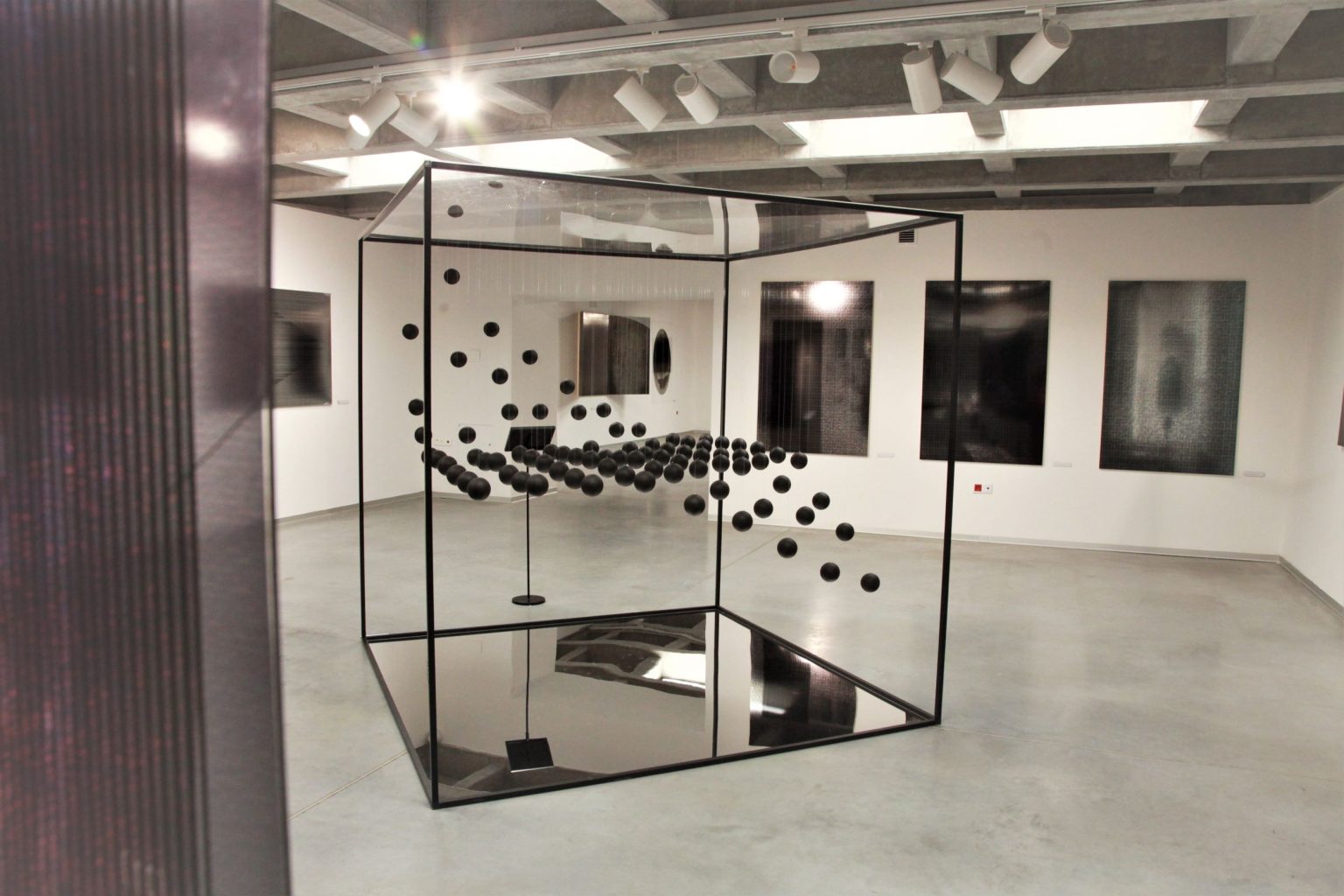 Duży szklany sześcian wypełniony czarnymi kulami, eksponowany w centralnej części sali wystawowej.