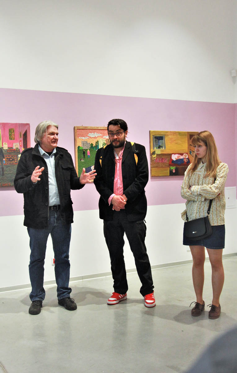 Trzy osoby stoją przed białą ścianą z zawieszonymi na niej obrazami.