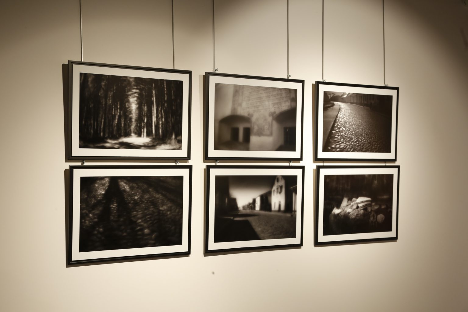 Przestrzeń wystawowa. Na ścianie wisi 6 oprawionych w ramy czarno-białych zdjęć