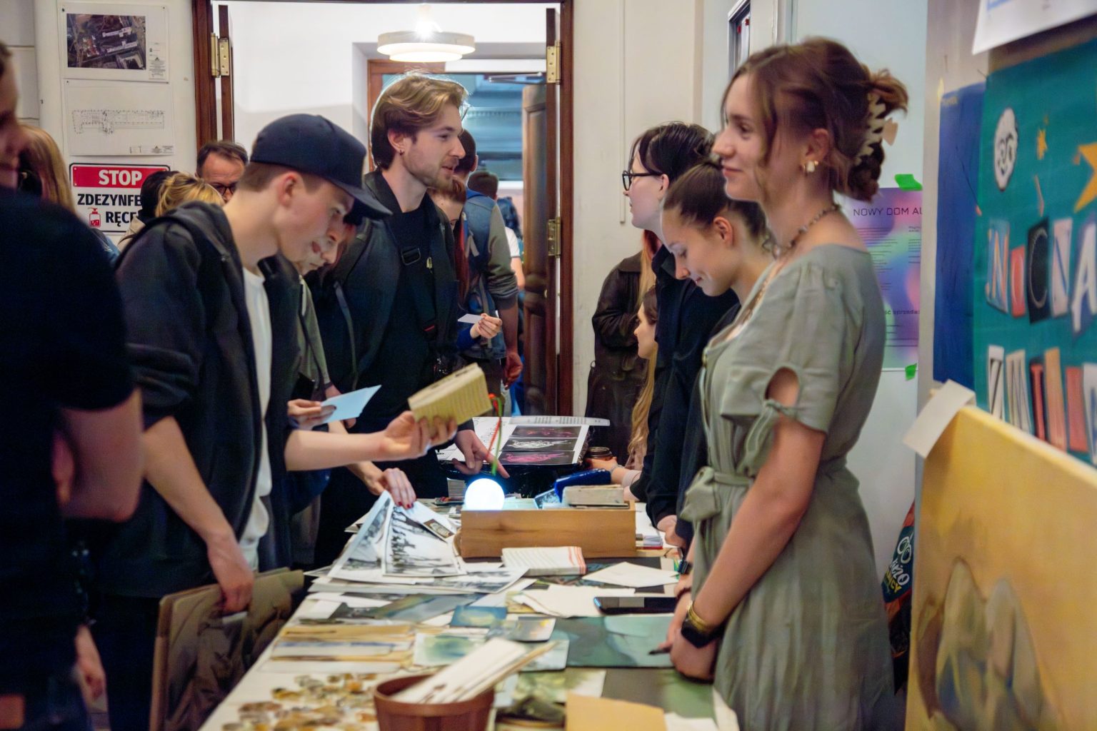Stoisko w budynku Wydziału Grafiki. Odwiedzający przeglądają prace wyłożone na stole
