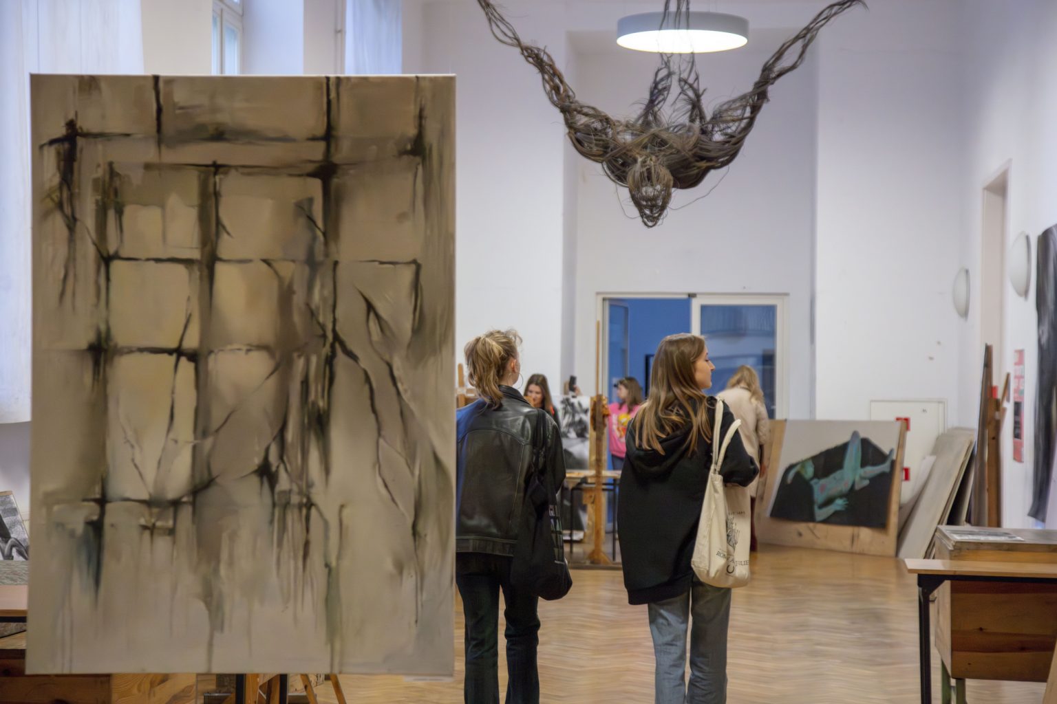 Dwie kobiety idą przez przestrzeń wystawową obserwując obrazy