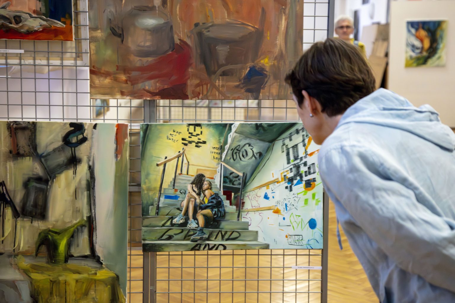 Kobieta obserwuje z bliska obraz przedstawiający dwie dziewczyny siedzące na schodach