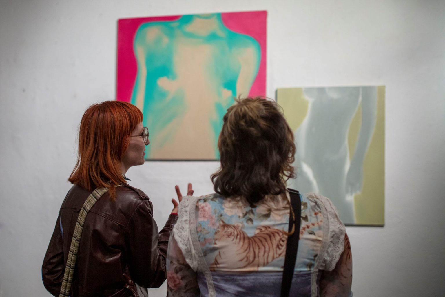 2 kobiety rozmawiają patrząc na powieszone na ścianie akty