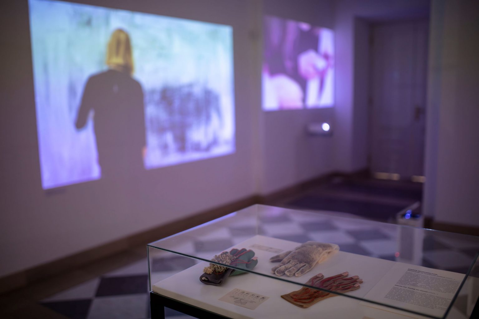 Gablota na środku sali, w której są eksponowane rękawice. W tle na ścianie wyświetlone zdjęcia z projektora.