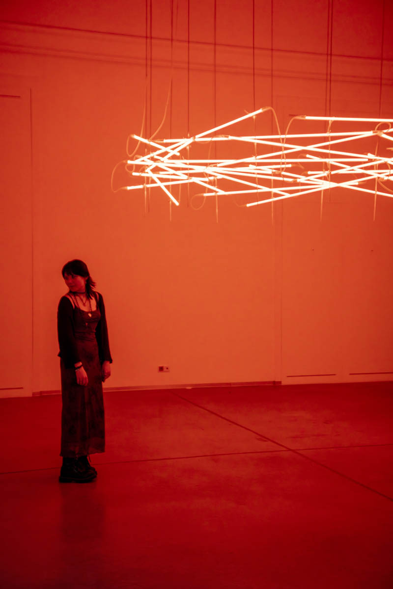 Kobieta stoi w oświetlonej na czerwono sali. Pod sufitem święcą jarzeniówki