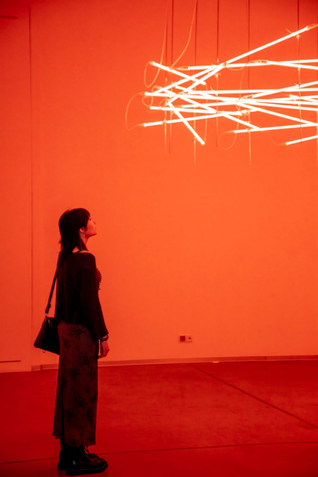 Kobieta w sali obserwuje podwieszone pod sufitem świetlówki ułożone w nieregularny wzór