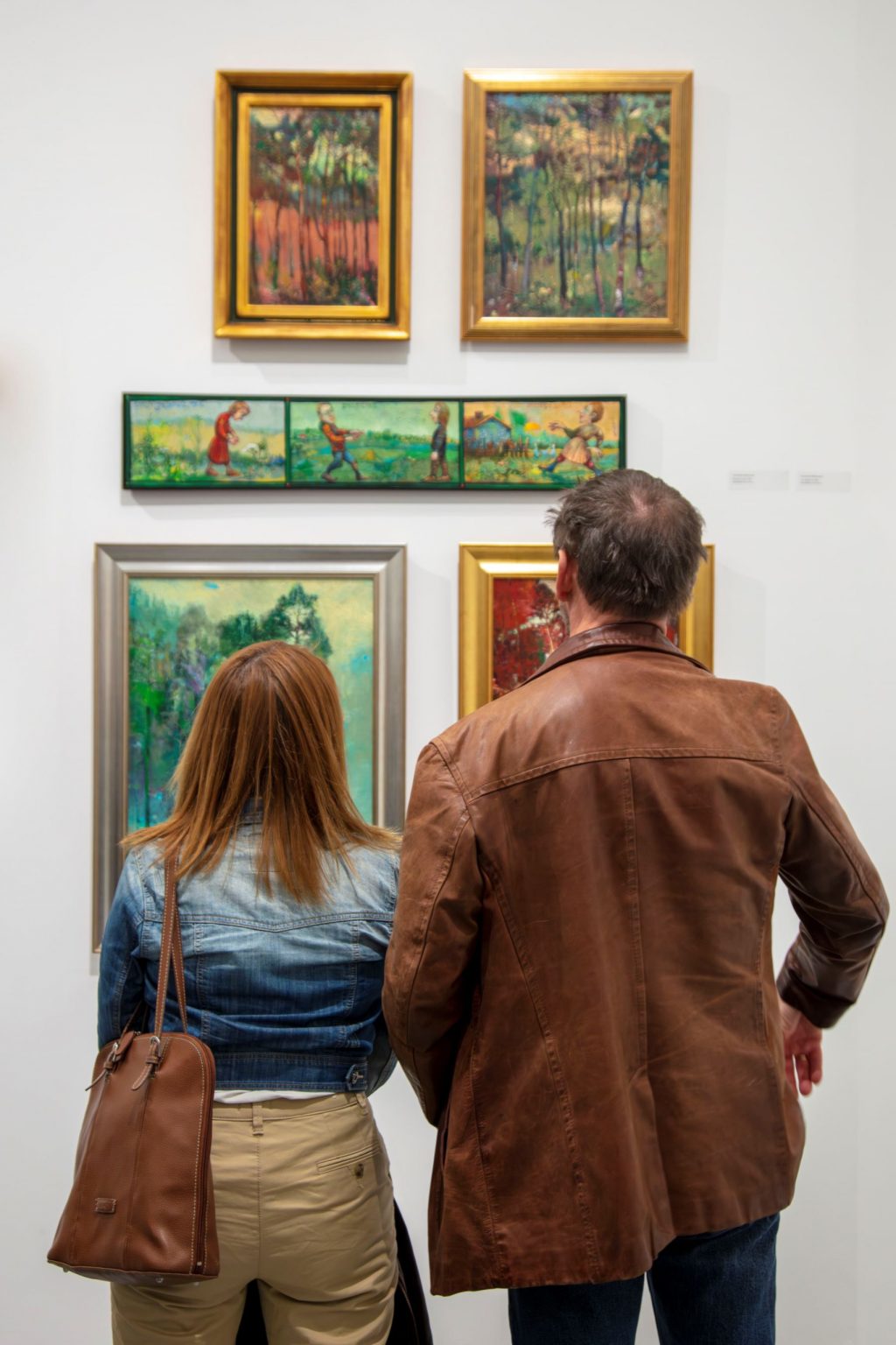 Kobieta i mężczyzna obserwują zawieszone na ścianie obrazy.