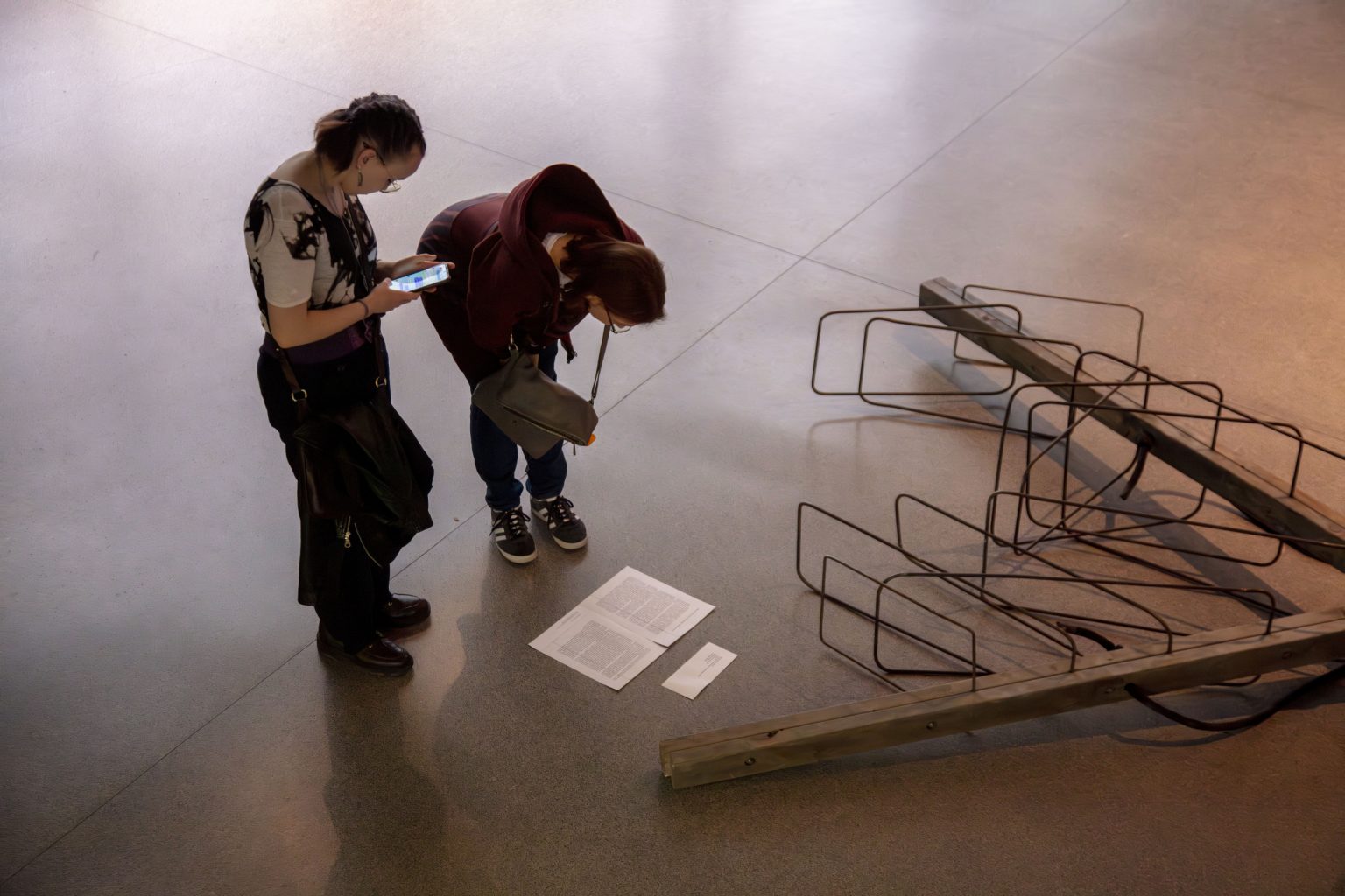 Dwie kobiety czytają opis leżącej na podłodze abstrakcyjnej rzeźby