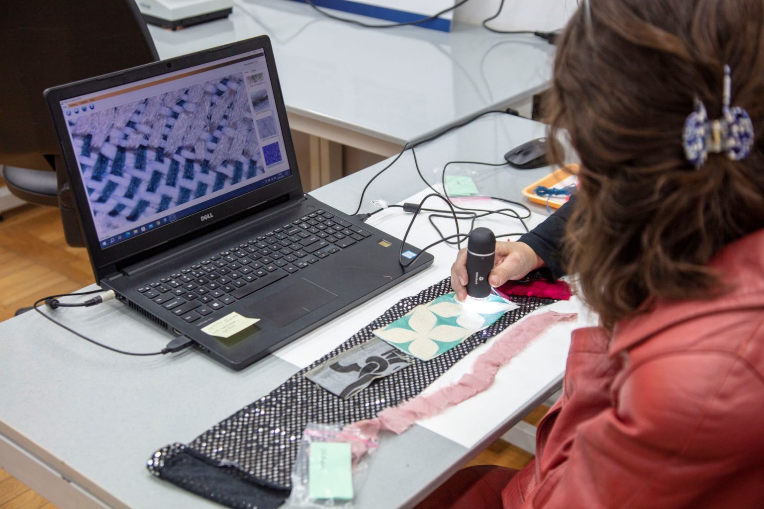 Kobieta siedzi przed laptopem obserwując wyświetlany na ekranie obraz pochodzący z trzymanego w ręku skanera