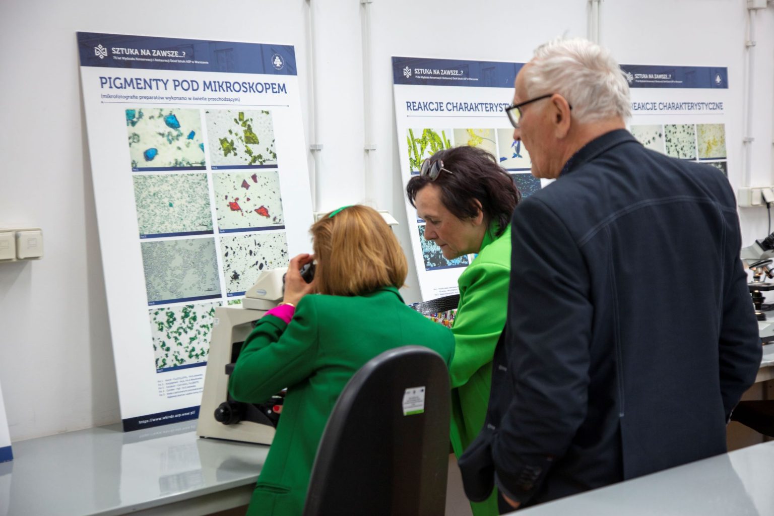 Kobieta siedzi przy mikroskopie, obo mężczyzna i kobieta przed tablicą z tytułem "Pigmenty pod mikroskopem"