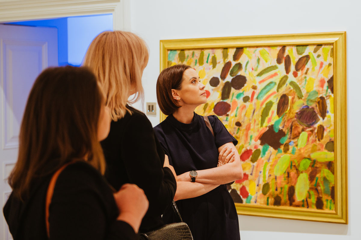 Osoby zwiedzające wystawę na tle obrazu