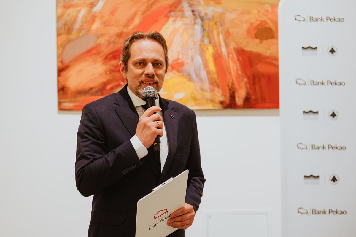 Mężczyzna mówi do mikrofonu. Obraz w tle