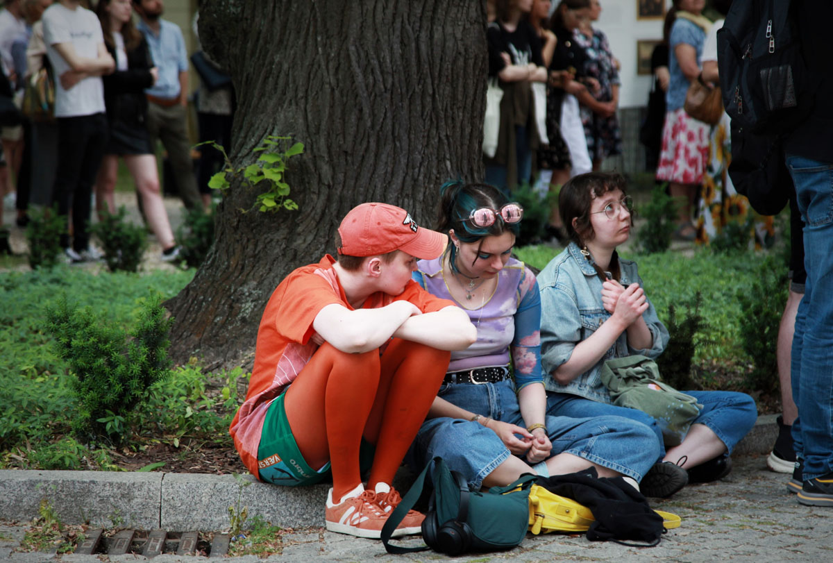 Trzy kolorowo ubrane dziewczyny siedzą pod drzewem na dziedzińcu pałacu