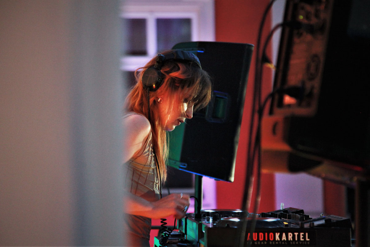 Didżejka w słuchawkach na uszach stoi za konsoletą