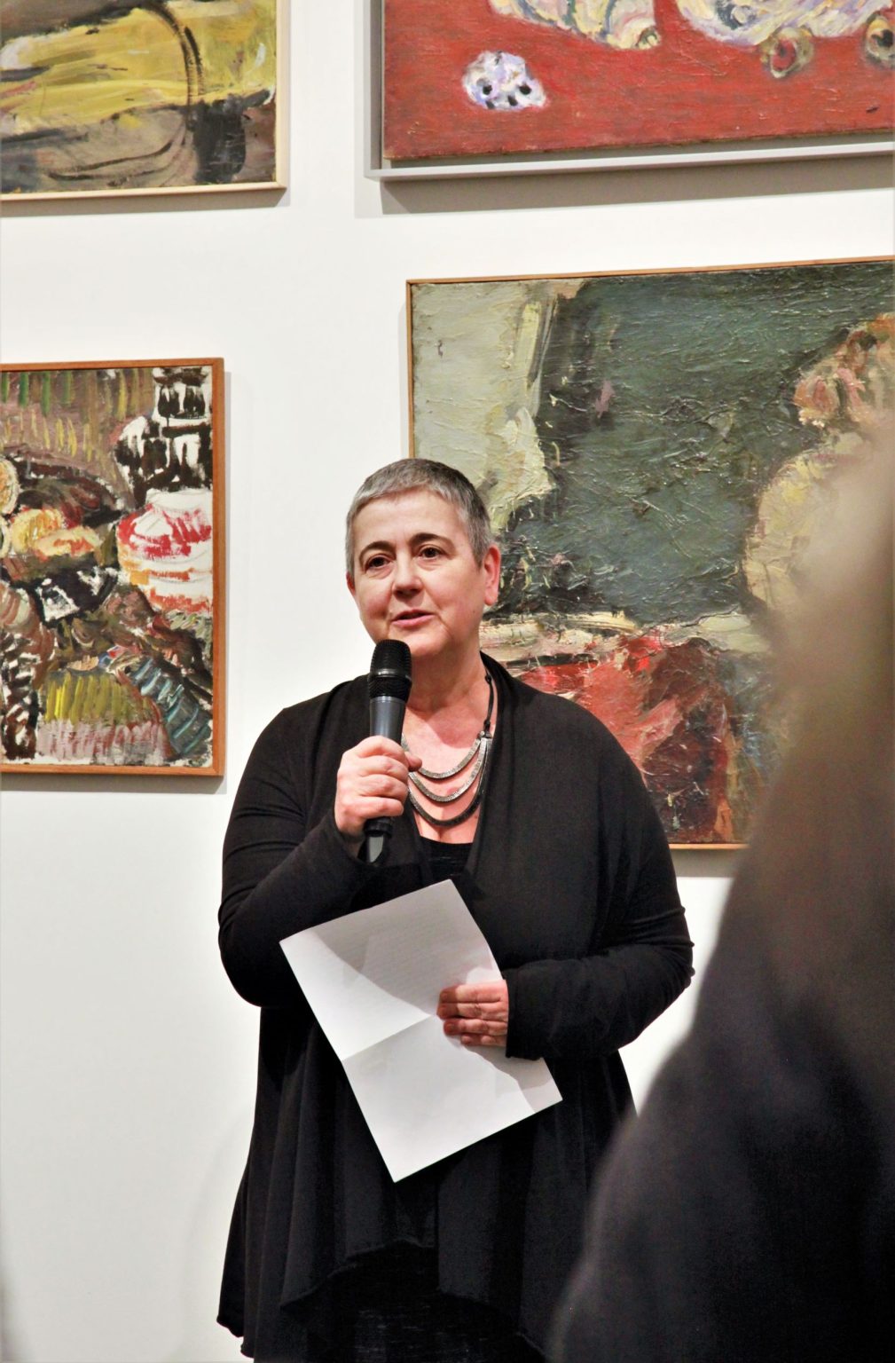 Wernisaż wystawy "(Nie)obowiązkowe nauczanie kapizmu", Dr Jolanta Gola stoi z mikrofonem w ręku, za nią widać ekspozycję