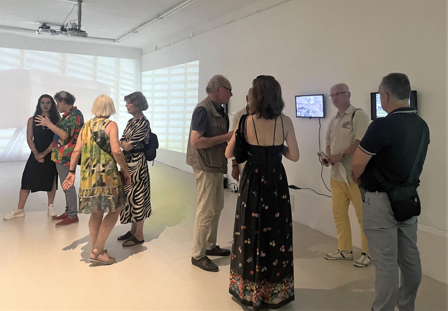 Grupa ludzi stojących w sali wystawowej na białej ścianie wyświetlany jest obraz z projektora