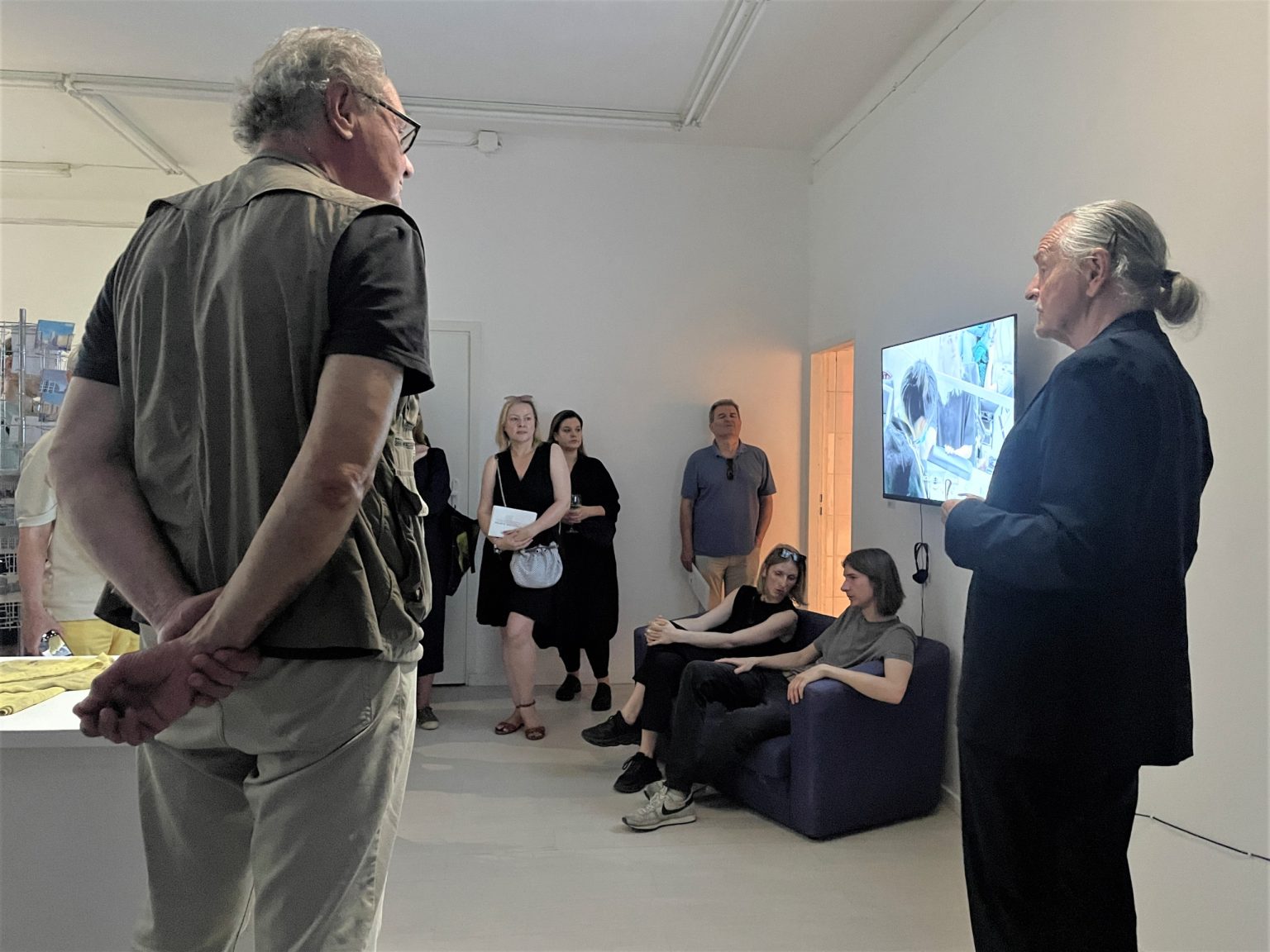 Grupa ludzi w przestrzeni wystawowej, kobieta i mężczyzna siedzą na kanapie