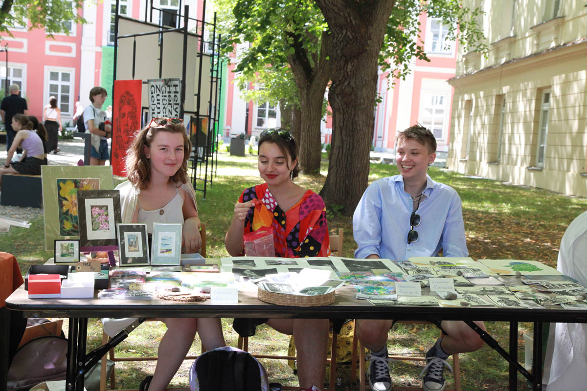 Na dziedzińcu Pałacu Czapskich za stołem z wyłożoną ekspozycją siedzą 2 dziewczyny i chłopak