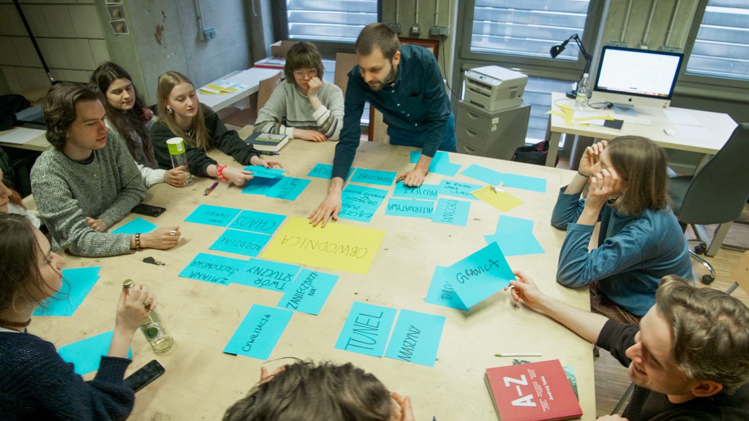 Studenci podczas zajęć siedzą wokół stołu w pracowni.