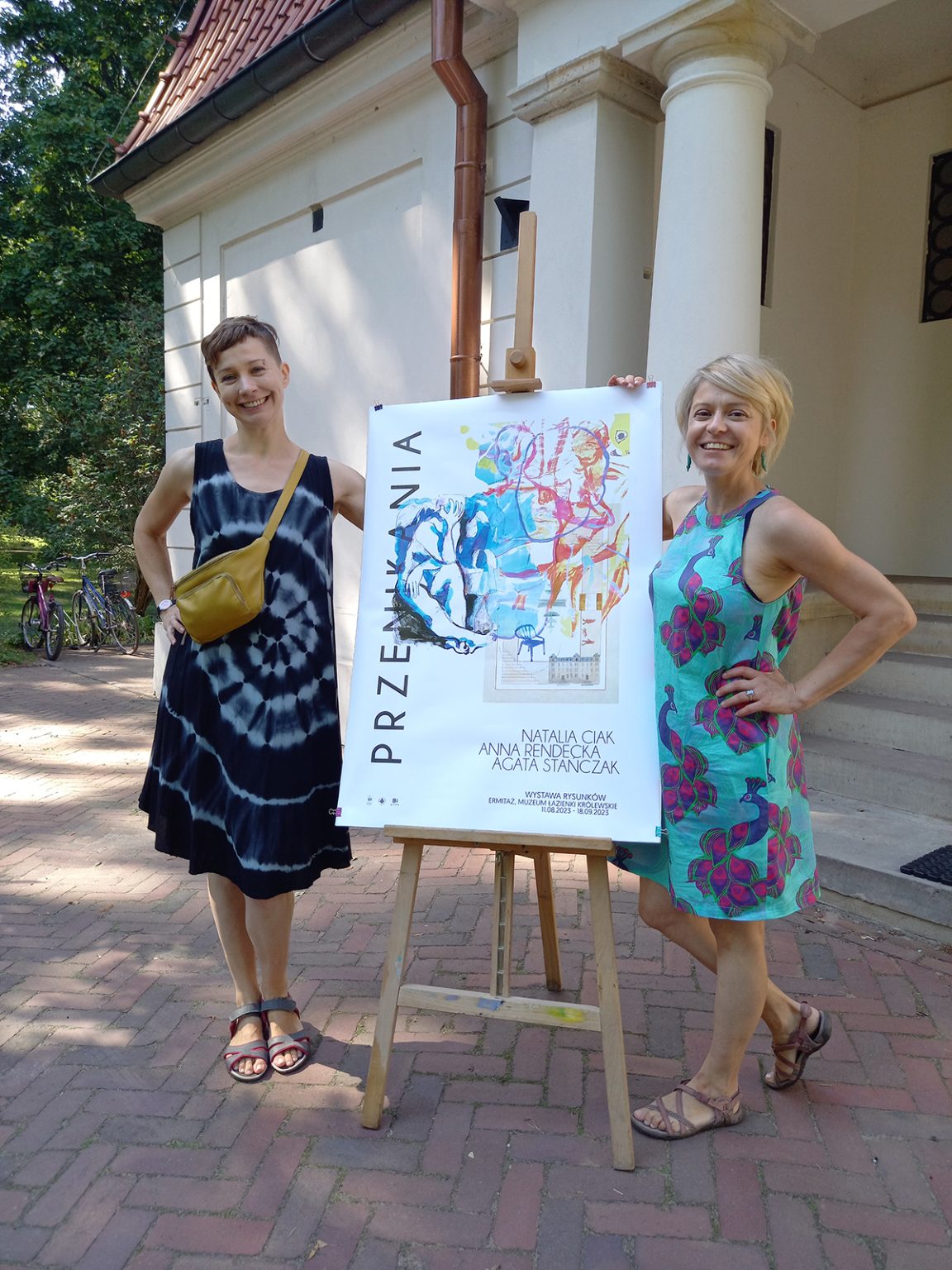 Artystki Natalia Ciak i Anna Rendecka przy plakacie wystawy przed wejściem do galerii Ermitaż, Muzeum Łazienki Królewskie. Fot. Przemek Powałko