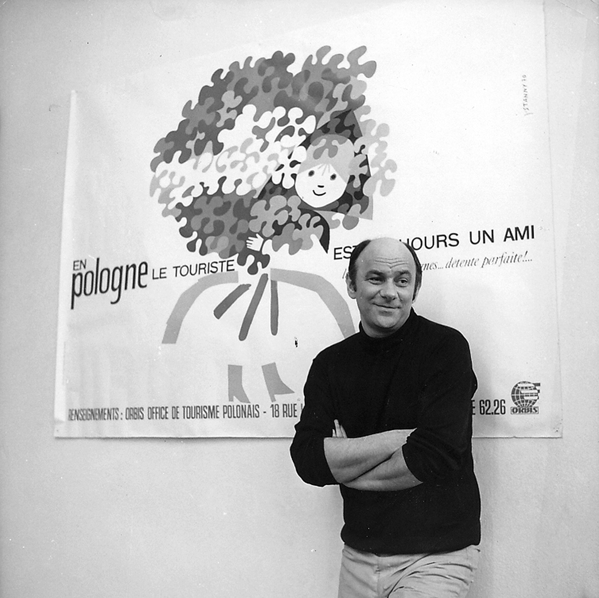 Janusz Stanny oparty o ścianę na której wisi jego plakat Orbisu