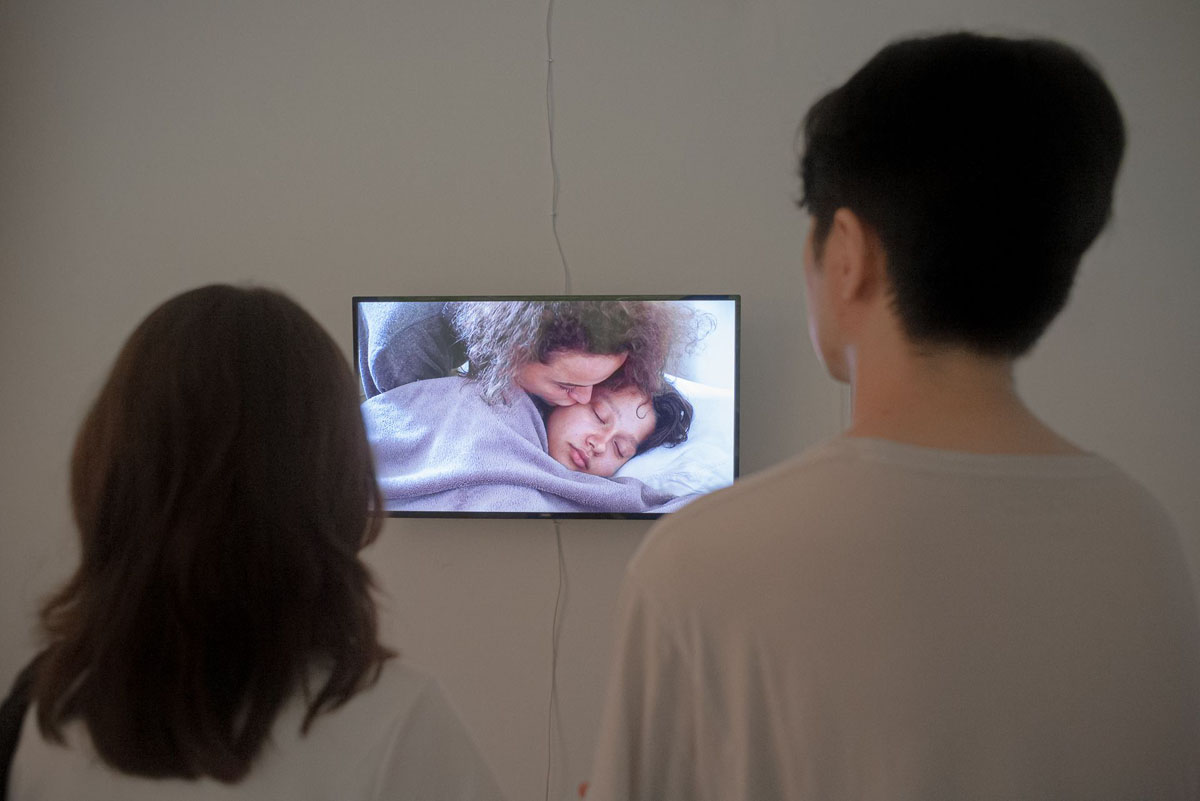 Dwie kobiety obserwują odtwarzany na monitorze obraz kobiety całującej śpiące dziecko