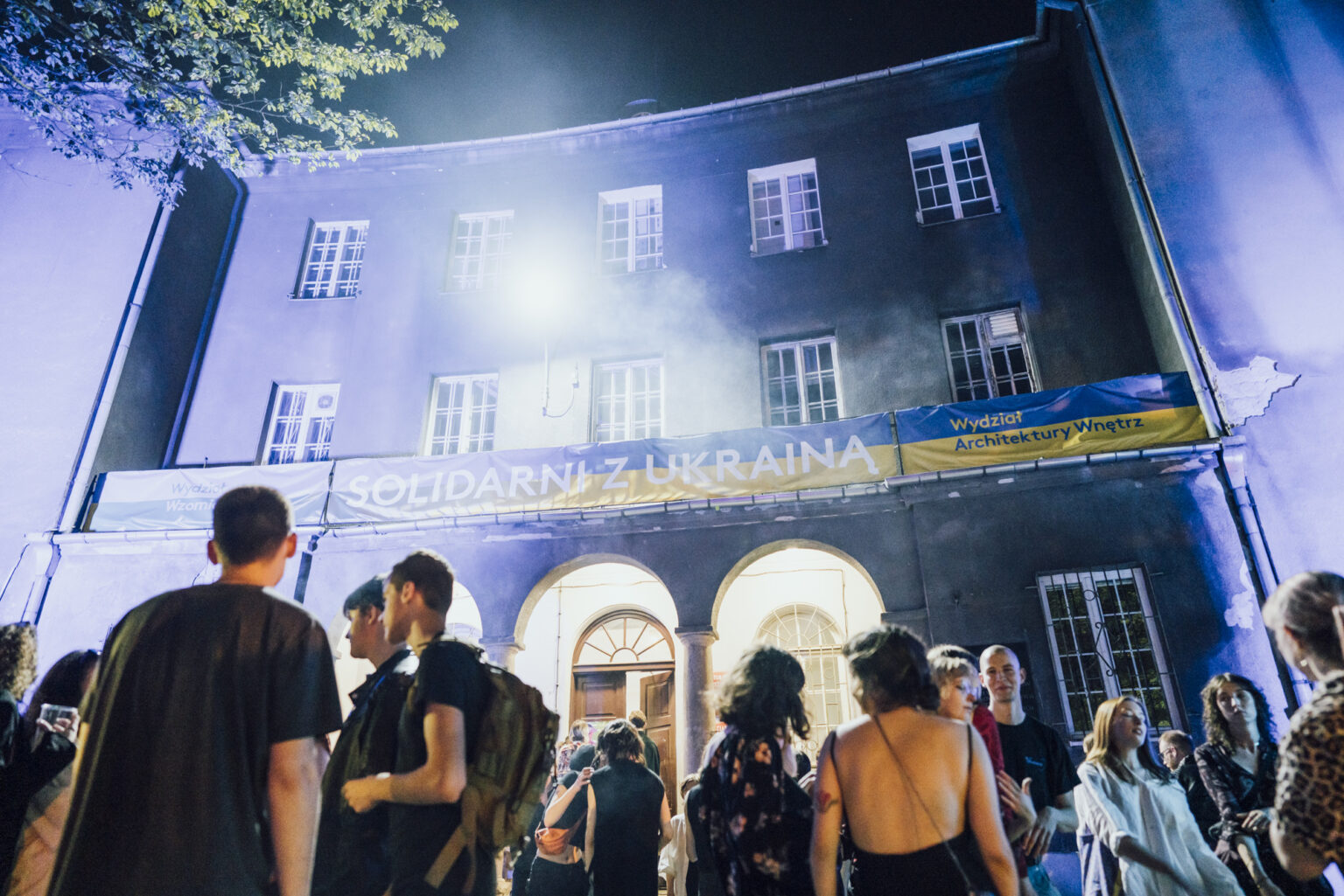 Grupa studentów i studentek na tle podświetlonego nocą budynku