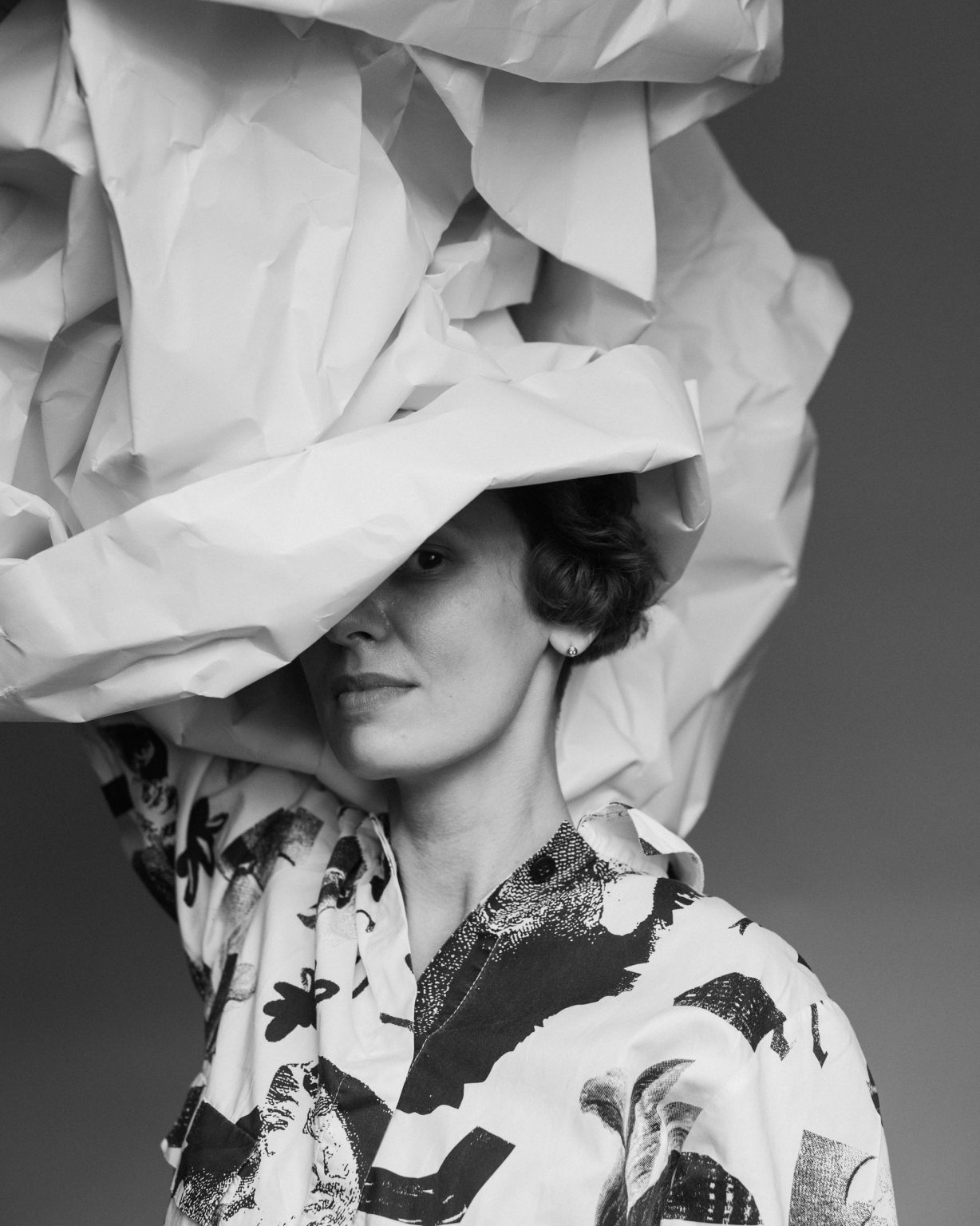 Kobieta ręką trzyma nad głową pognieciony rulon papieru zasłaniającego jej oko