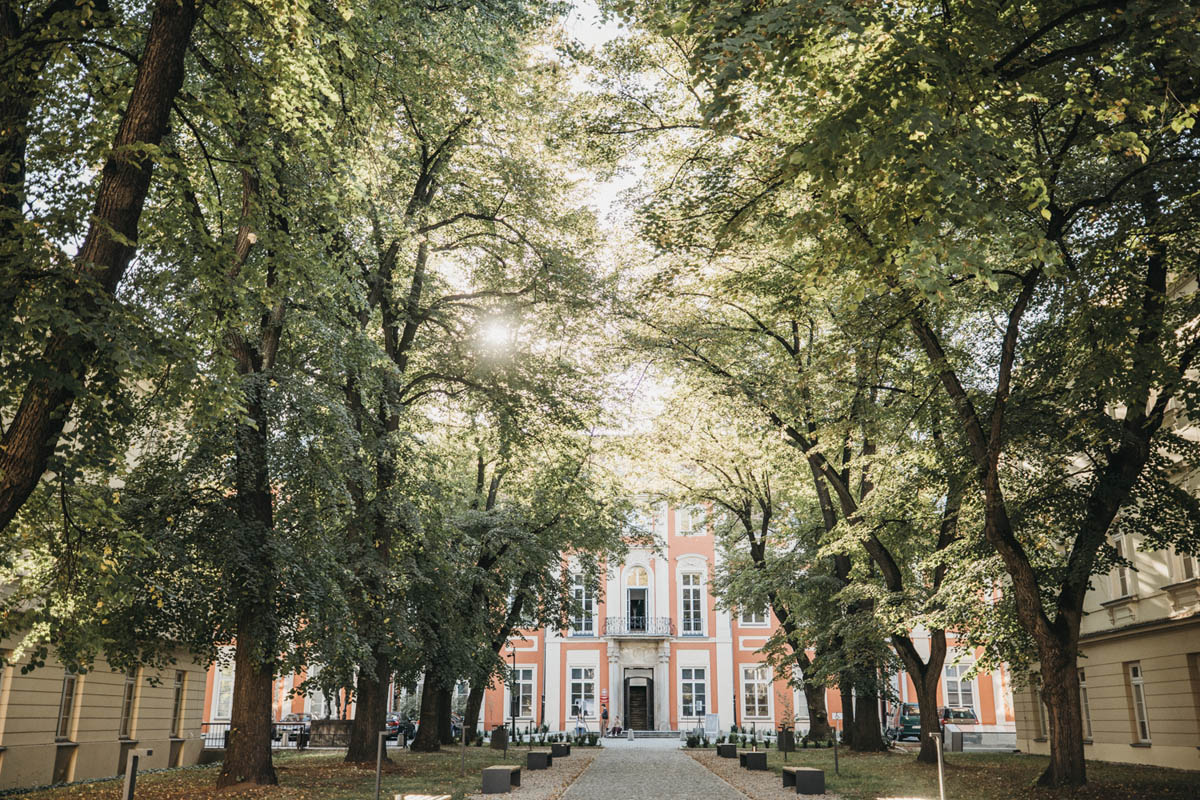 Fasada Pałacu Czapskich przesłonięta drzewami stojącymi na dziedzińcu