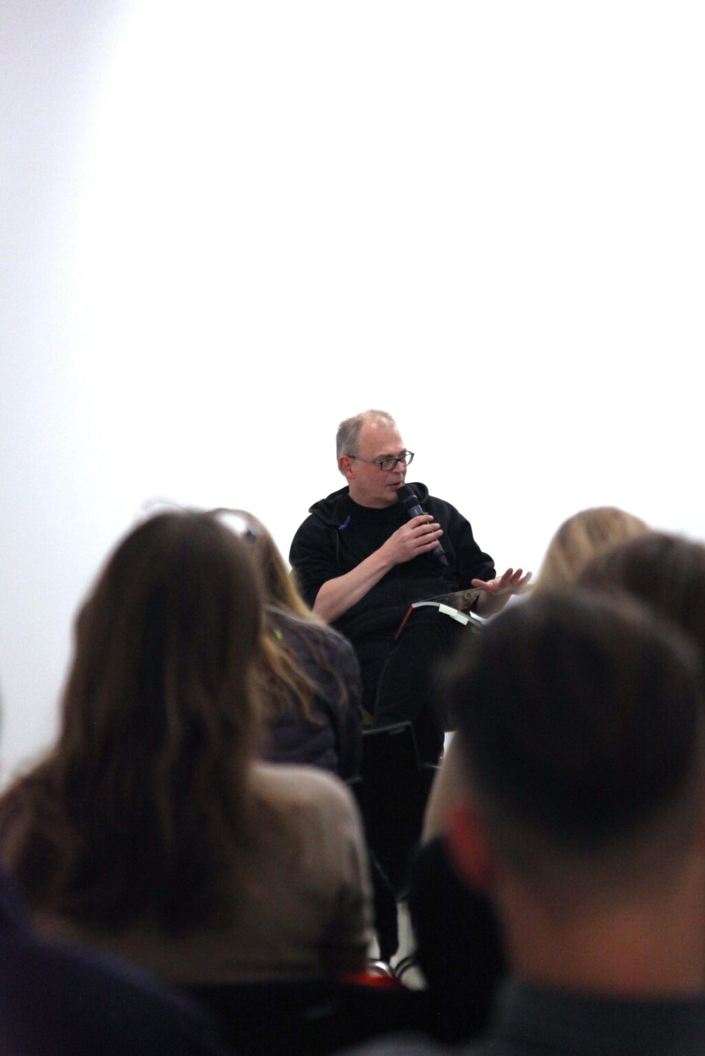 Sylwetki osób. W tle mężczyzna mówiący do mikrofonu