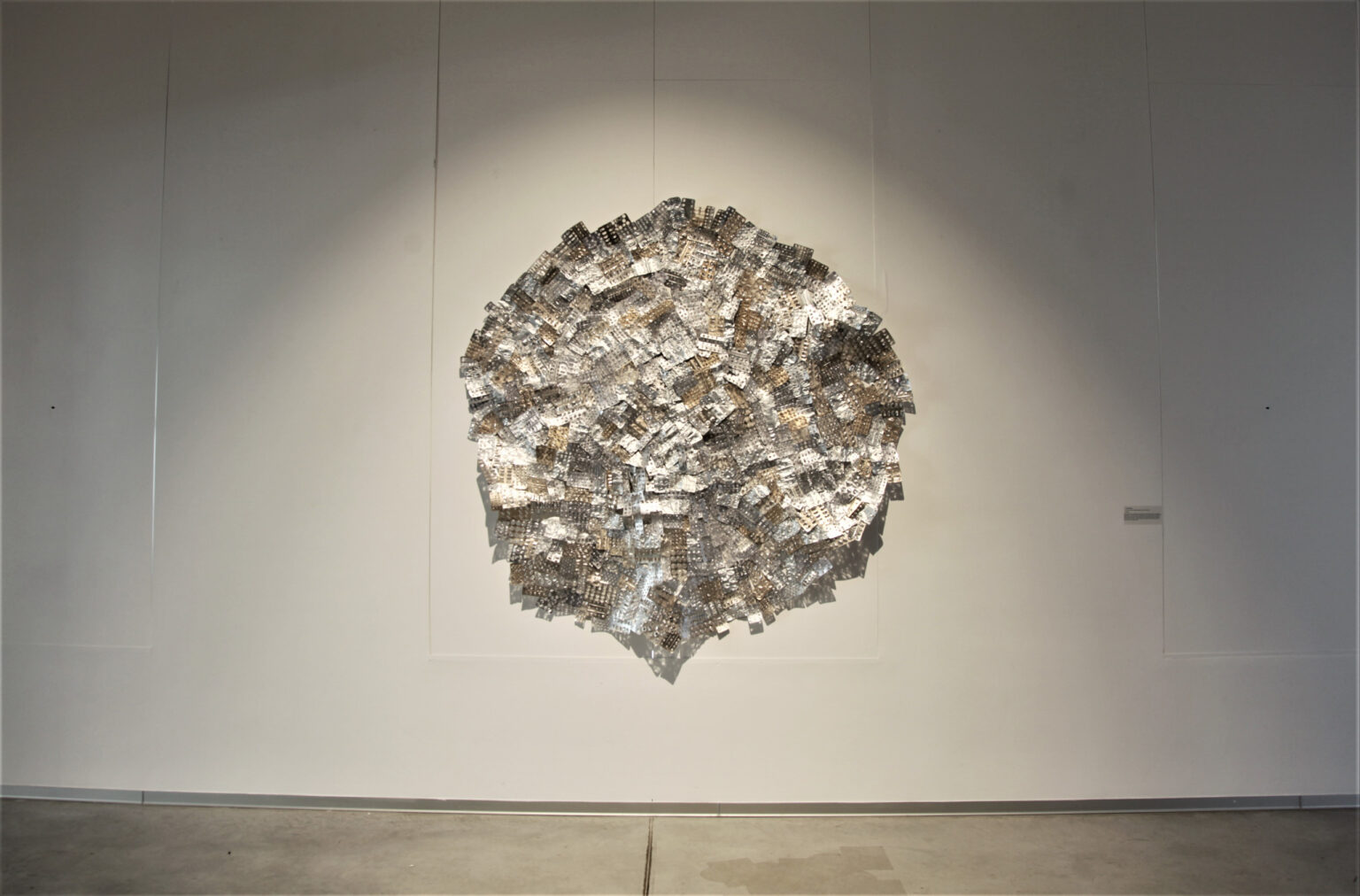 Duży okrąg wykonany ze srebrnych i złotych elementów na białej ścianie.