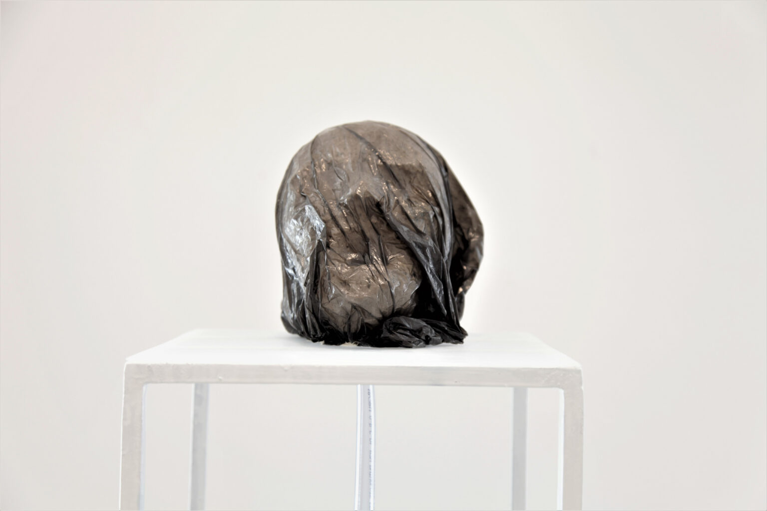 Rzeźba pokryta czarną folią przez którą widać delikatny zarys ludzkiej twarzy