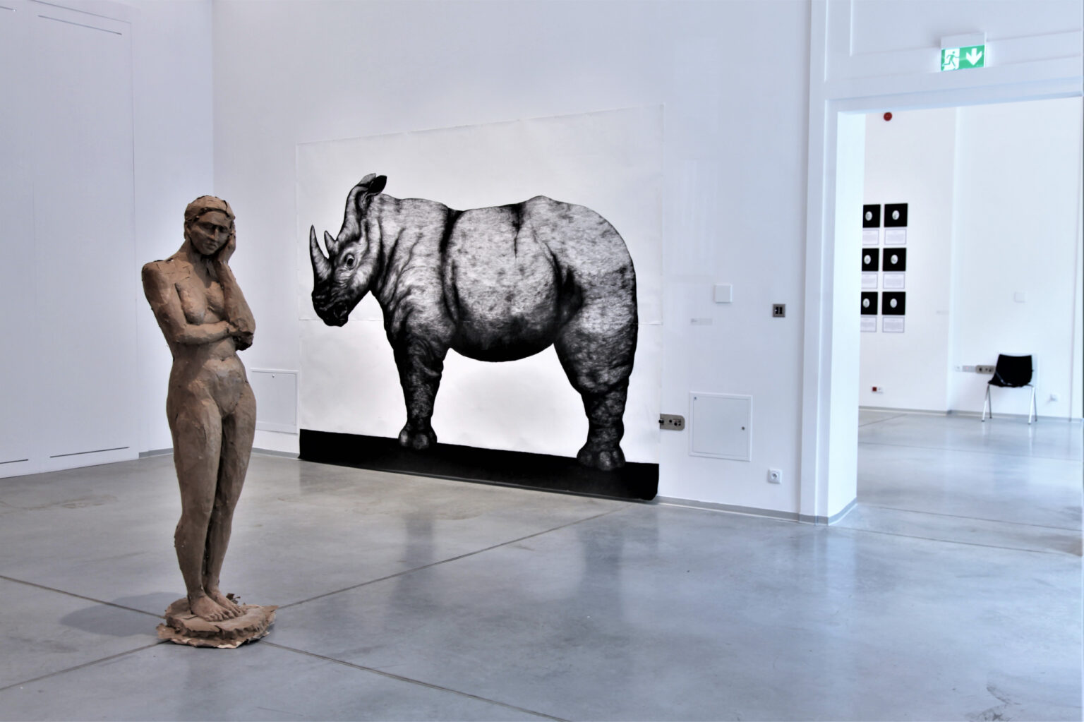 Stojąca pośrodku sali rzeźba kobiety na ścianie wisi naszkicowany nosorożec