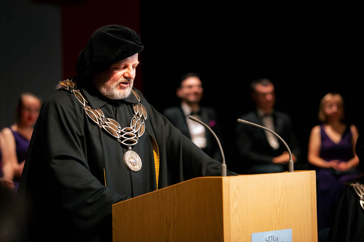 Mężczyzna w uroczystej todze i insygniach akademickich na mównicy